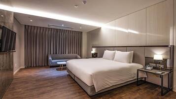 Una habitación de hotel moderna con una cama grande, un sofá, una mesita y un televisor.