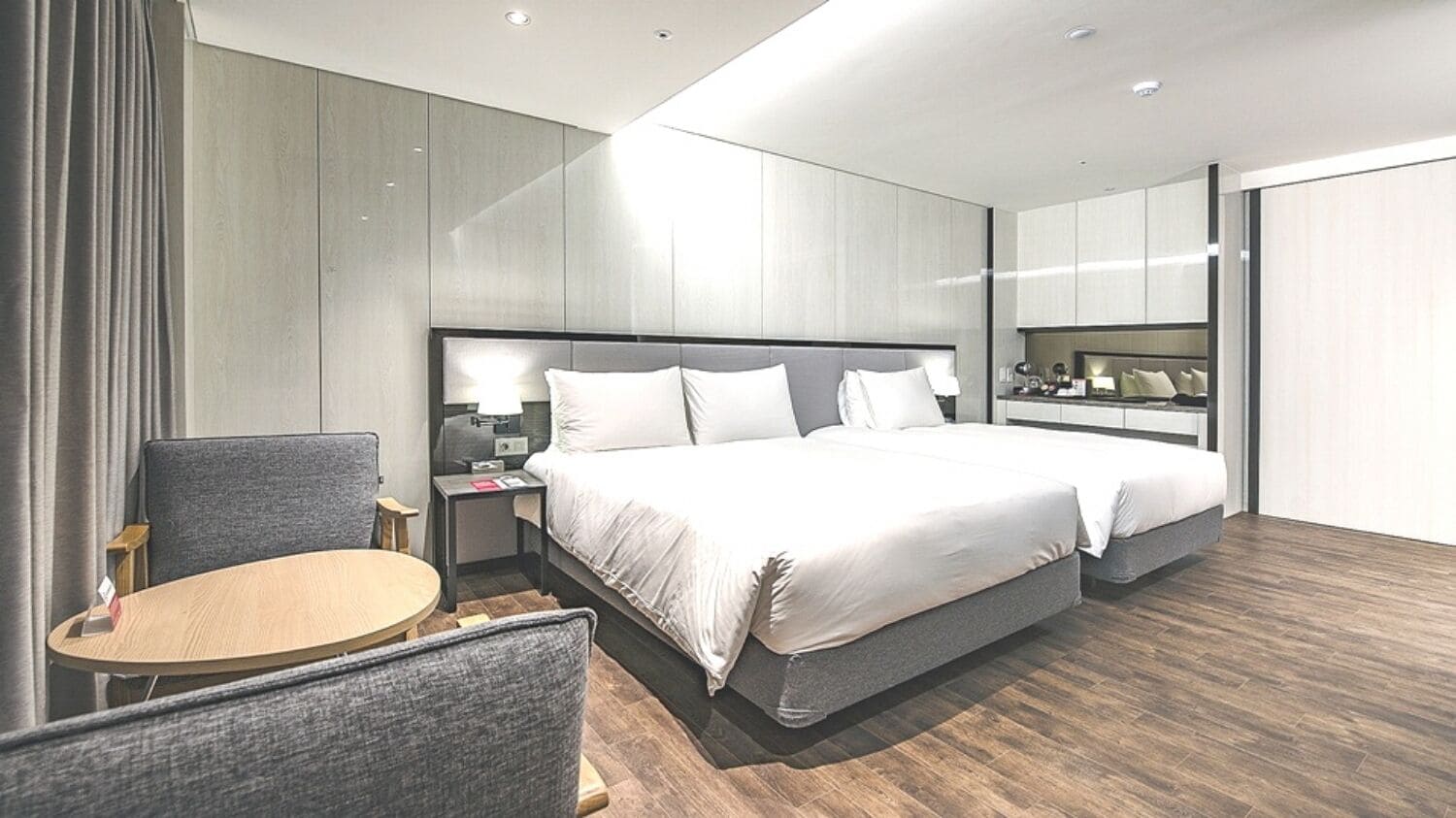 A modern hotel room with a large bed, bedside tables, a chair, and a small table.