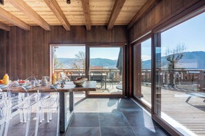 Eine moderne Küche mit Holzbalkendecke, großen Fenstern und einem Essbereich mit klaren Stühlen.