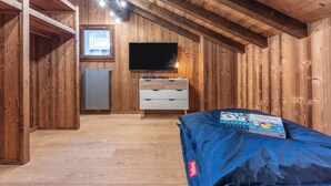A room with wooden walls and a sloped ceiling, a flat-screen TV mounted on the wall, a white dresser with drawers, and a blue mattress on the floor. - Chalet 1907 (Gérardmer)