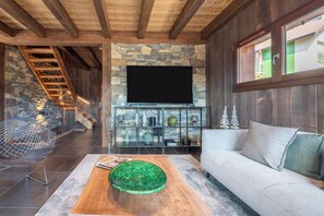 Ein modernes Wohnzimmer mit Kamin aus Stein, einem Flachbildfernseher, einer Holztreppe und einem Sofa.