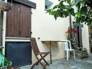 A patio with a wooden table and chairs, a white plastic chair, a wooden door, and a plant with red flowers. - Schönes Ferienhaus mit Garten und Whirlpool by Interhome (Testico)