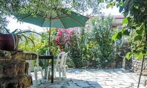 An outdoor patio with a table and chairs, surrounded by greenery and a stone wall. - Schönes Ferienhaus mit Garten und Whirlpool by Interhome (Testico)