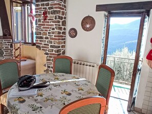 A dining area with a table covered in a floral tablecloth, surrounded by chairs with cushioned seats. A radiator is visible beneath the table, and a window with a view of trees and mountains is in the background. - Schönes Ferienhaus mit Garten und Whirlpool by Interhome (Testico)