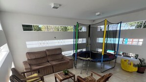 A spacious living area with a sofa, wooden chairs, a trampoline, and a potted plant. - Comfortable house with pool and 4 suites. Close to everything. Super quiet place. (Piranhas)