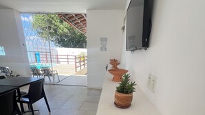 A room with a tiled floor, a white wall-mounted TV, a dining area with chairs and a table, and a potted plant with a cactus. - Comfortable house with pool and 4 suites. Close to everything. Super quiet place. (Piranhas)