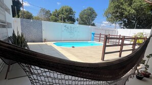 A hammock over a tiled patio with a swimming pool in the background. - Comfortable house with pool and 4 suites. Close to everything. Super quiet place. (Piranhas)