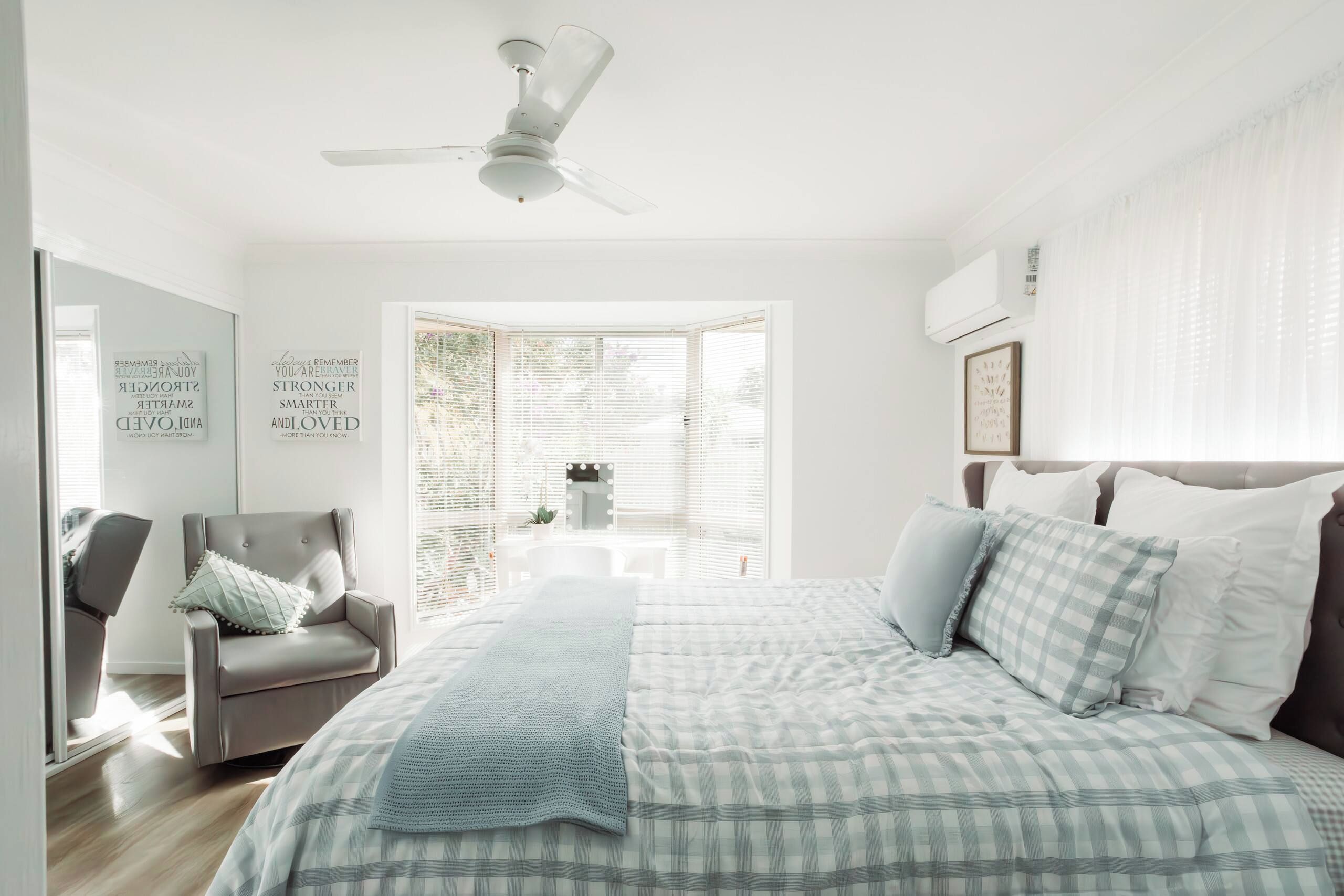 A bedroom with a bed, a chair, a ceiling fan, and a window with blinds.