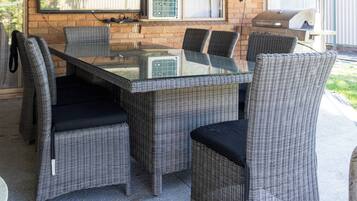 An outdoor patio with a glass-top table surrounded by wicker chairs, a ceiling fan, and string lights.