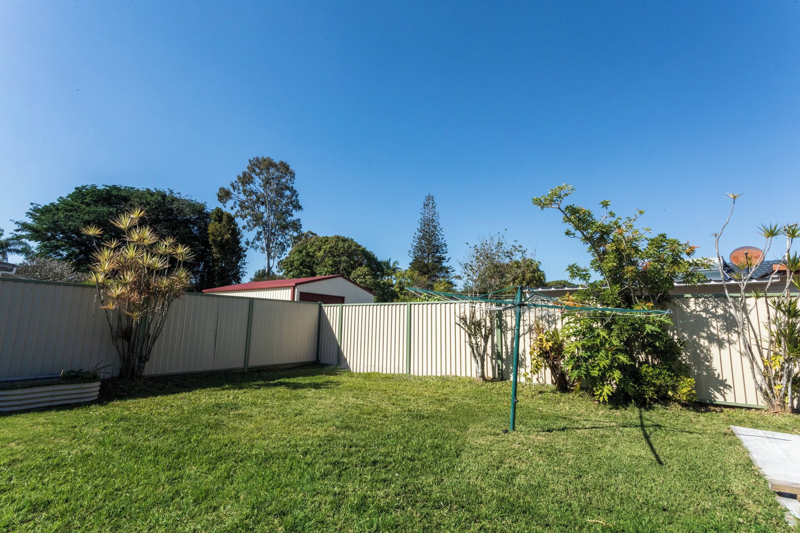 A backyard with a fenced area, a small shed, and a variety of trees and plants.
