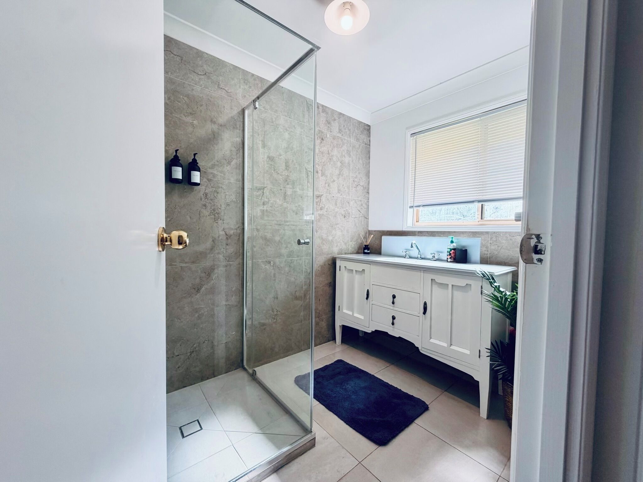 A modern bathroom with a glass shower enclosure, white cabinetry, and a window above the sink.