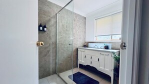 Une salle de bain moderne avec une douche à l’italienne en verre, des meubles blancs et une fenêtre au-dessus du lavabo.