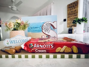 Un taulell de cuina amb un cartell de benvinguda, un paquet de galetes Arnott's Cream Favourites, un ram de flors i un cartell decoratiu amb la forma d'una rosa.