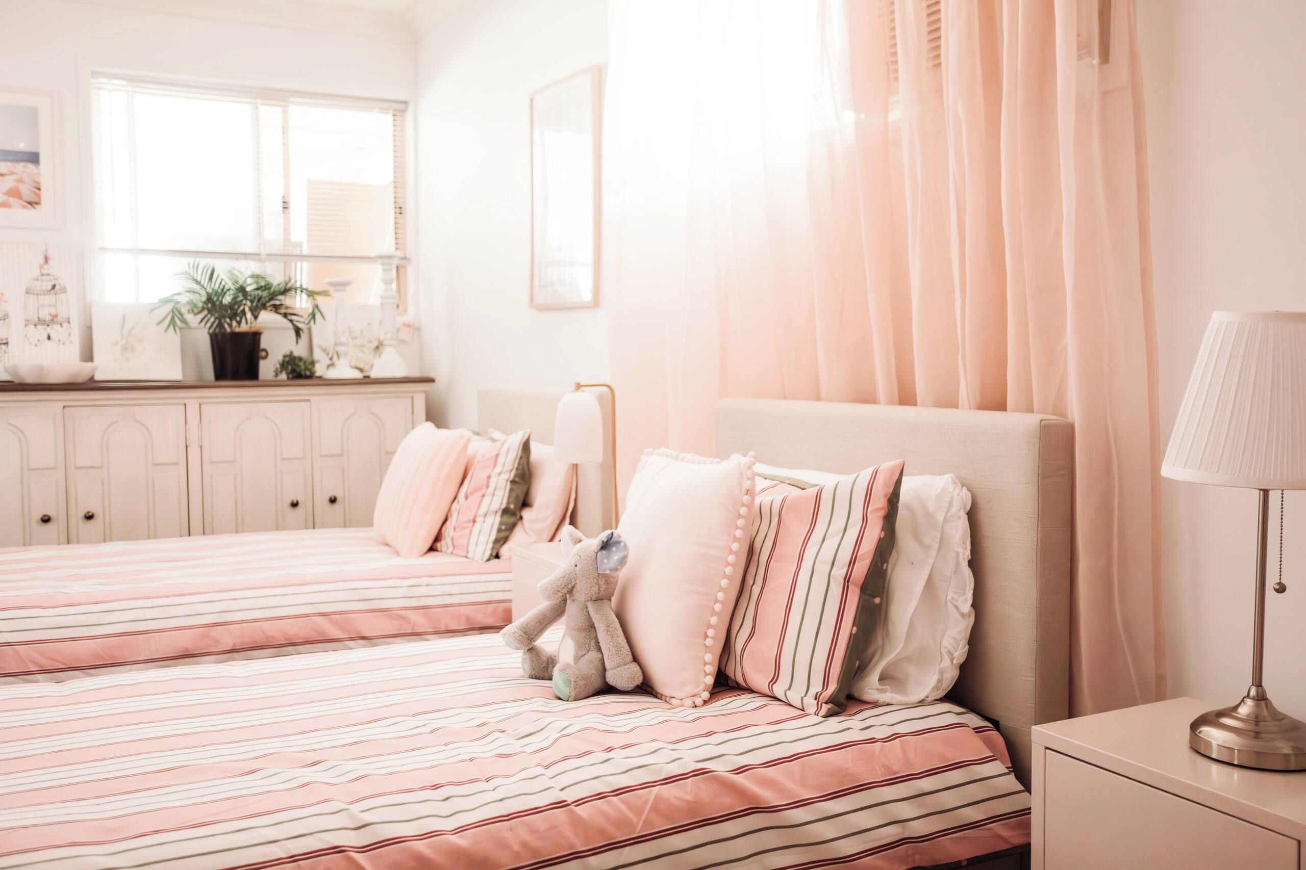 A bedroom with two beds, a nightstand, a lamp, and a window with curtains.