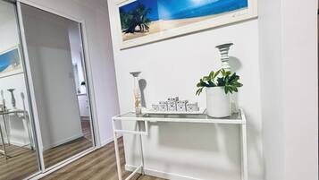 A room with a white console table, a framed picture of a beach, and a potted plant.