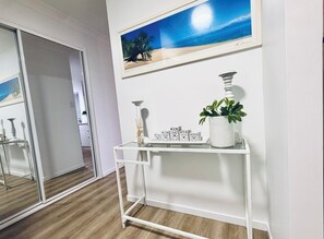 A room with a white console table, a framed picture of a beach, and a potted plant.