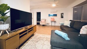 Un salon avec un téléviseur à écran plat posé sur un meuble en bois, un canapé foncé agrémenté d’un plaid, un tapis à motifs et un ventilateur de plafond.