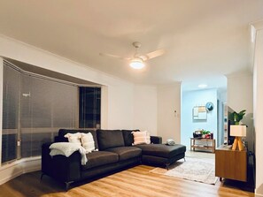A modern living room with a sectional sofa, a ceiling fan, and a view into the adjacent dining area.