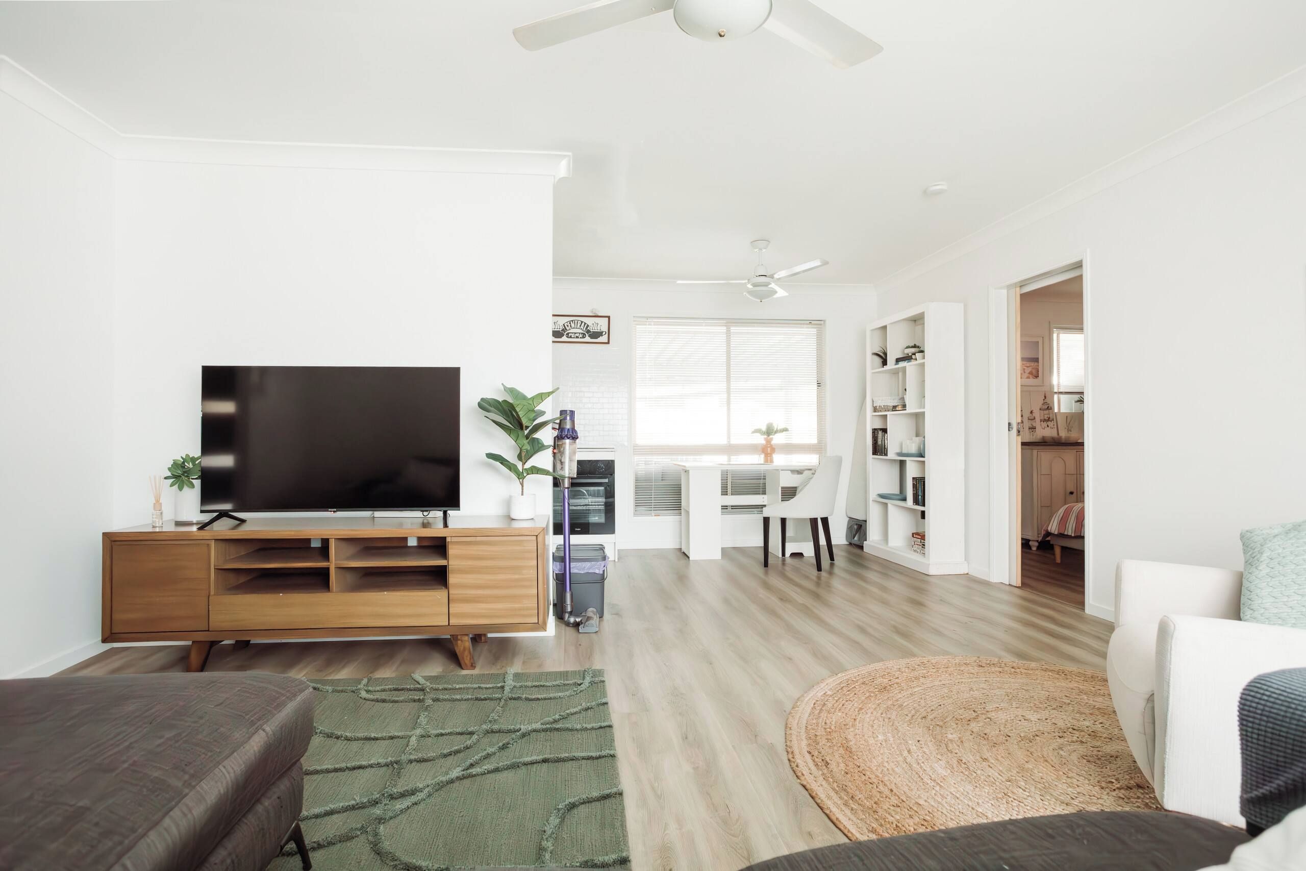 A modern living room with a flat-screen TV, wooden entertainment unit, and a green area rug.