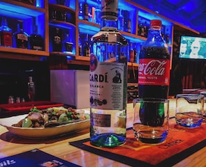 A bar setting with a bottle of Cardí, a bottle of Coca-Cola, and a plate of food. - Hotel 4 U Saliya Garden  (Anuradhapura)