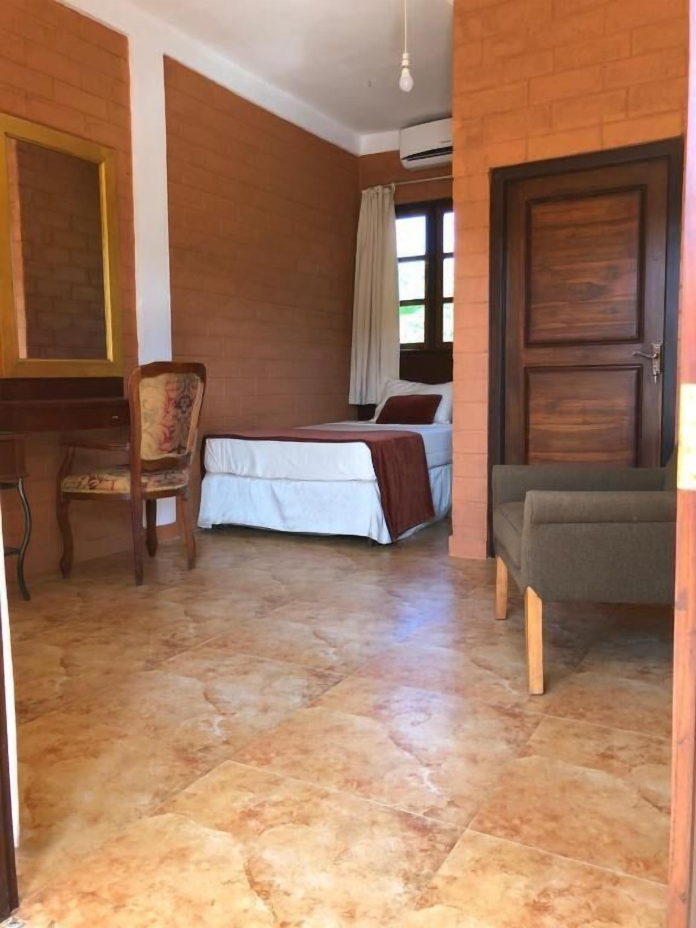 A room with a bed, a chair, a desk, and a door.