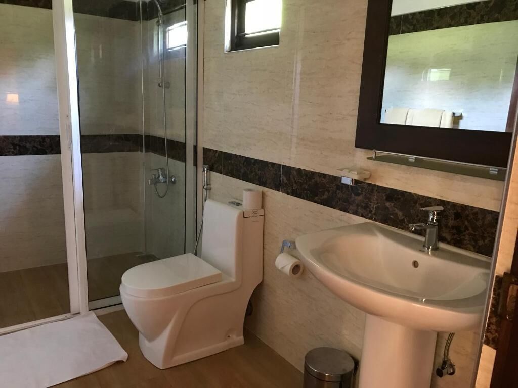 Un baño con ducha de vidrio, inodoro y lavamanos con espejo.