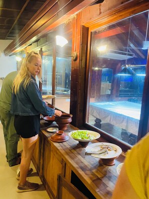 A person preparing food at a wooden counter with a window, a bowl, and a plate with food remnants. - Hotel 4 U Saliya Garden  (Anuradhapura)