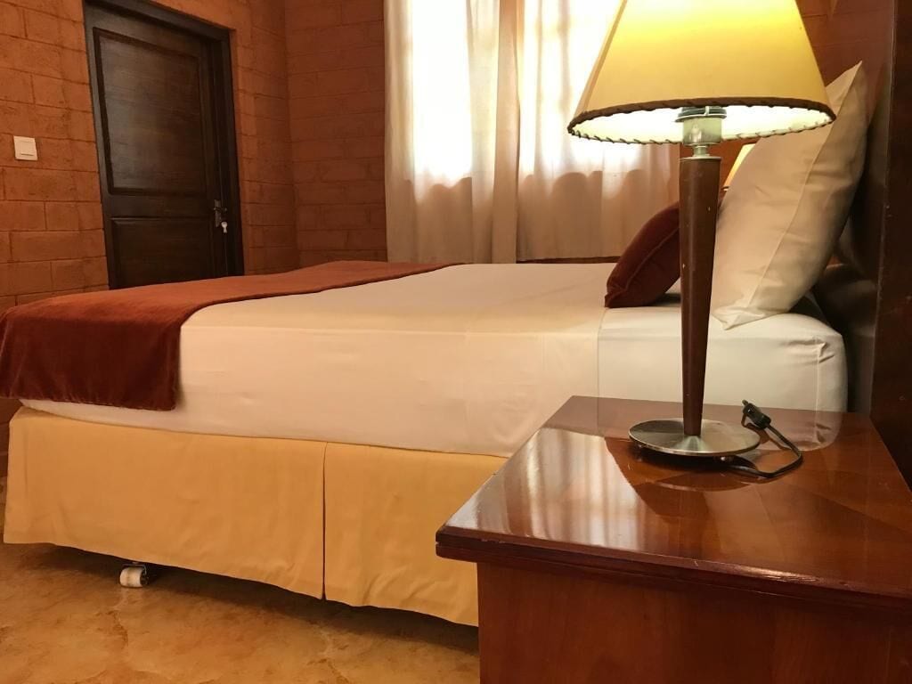 A hotel room with a bed, bedside table, lamp, and a door.