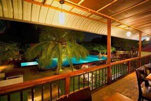 An outdoor pool area with a wooden deck, palm trees, and a covered seating area. - Hotel 4 U Saliya Garden  (Anuradhapura)