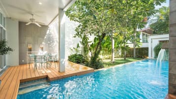 Una piscina con muelle de madera, una mesa y sillas, y un árbol.