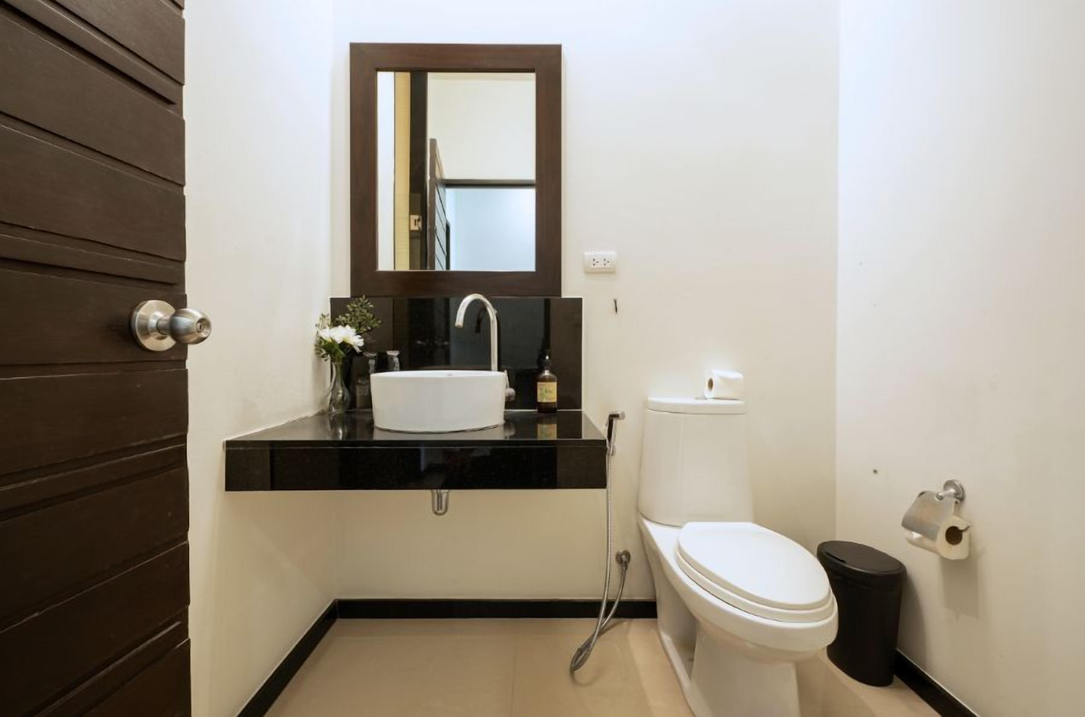 A compact bathroom with a white toilet, a black sink, and a mirror above it.
