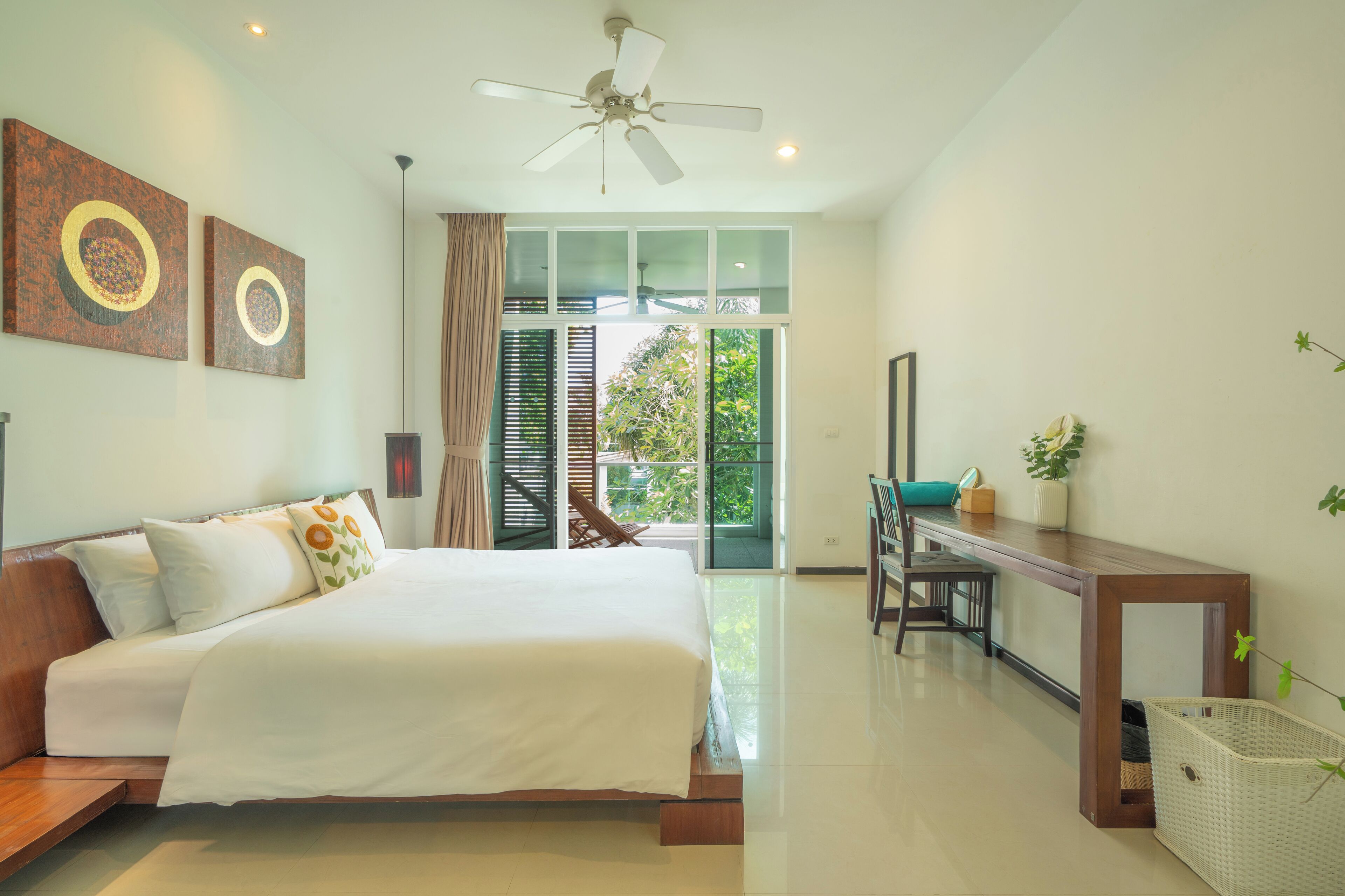 A bedroom with a bed, a desk, a chair, a ceiling fan, and a view of the outdoors.
