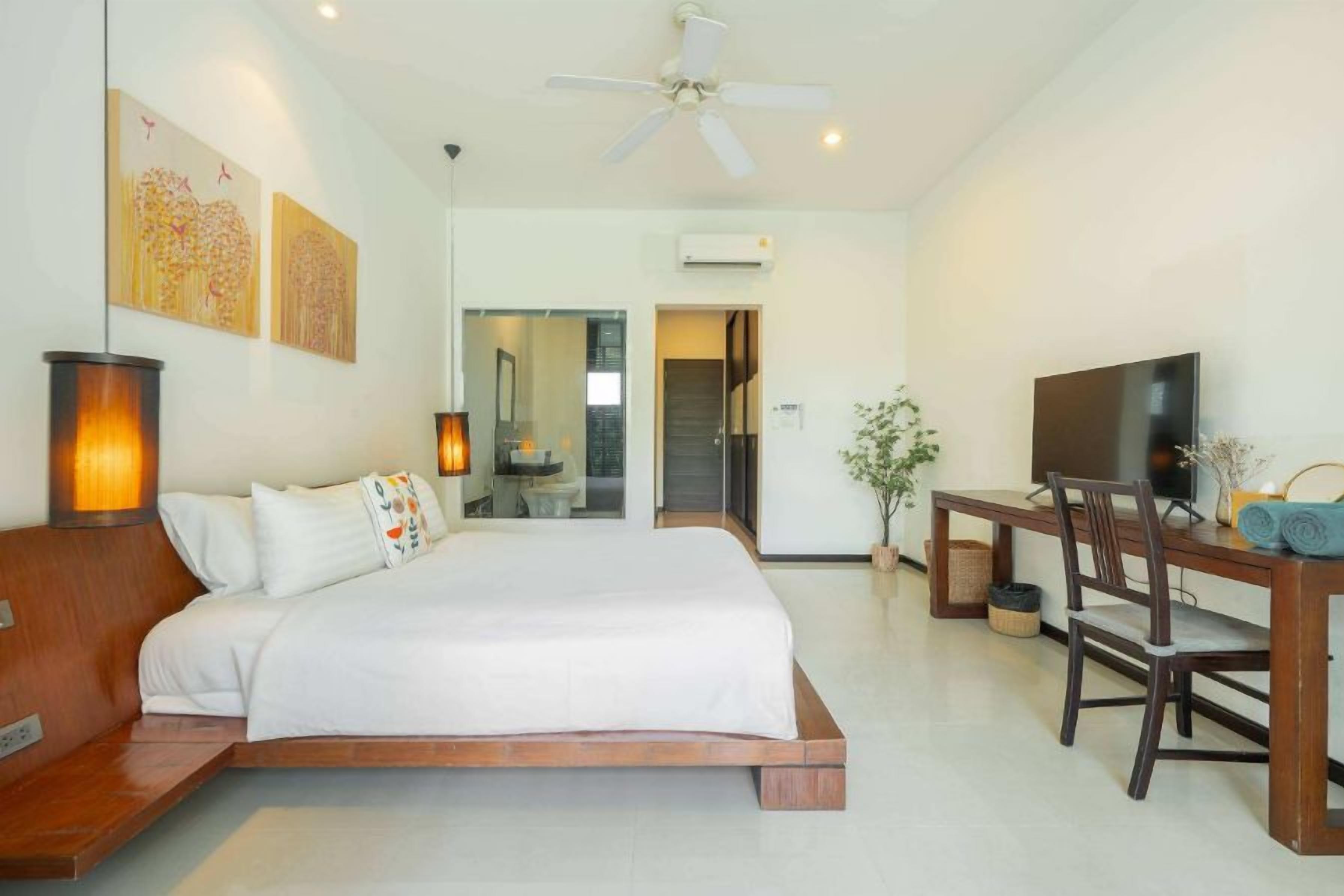 A bedroom with a bed, bedside table, lamp, TV, and a desk with chair.
