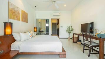 A bedroom with a bed, bedside table, lamp, TV, and a desk with chair.