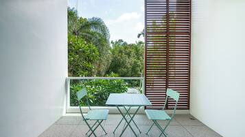 A balcony with a table and chairs, a view of greenery, and a window with blinds.