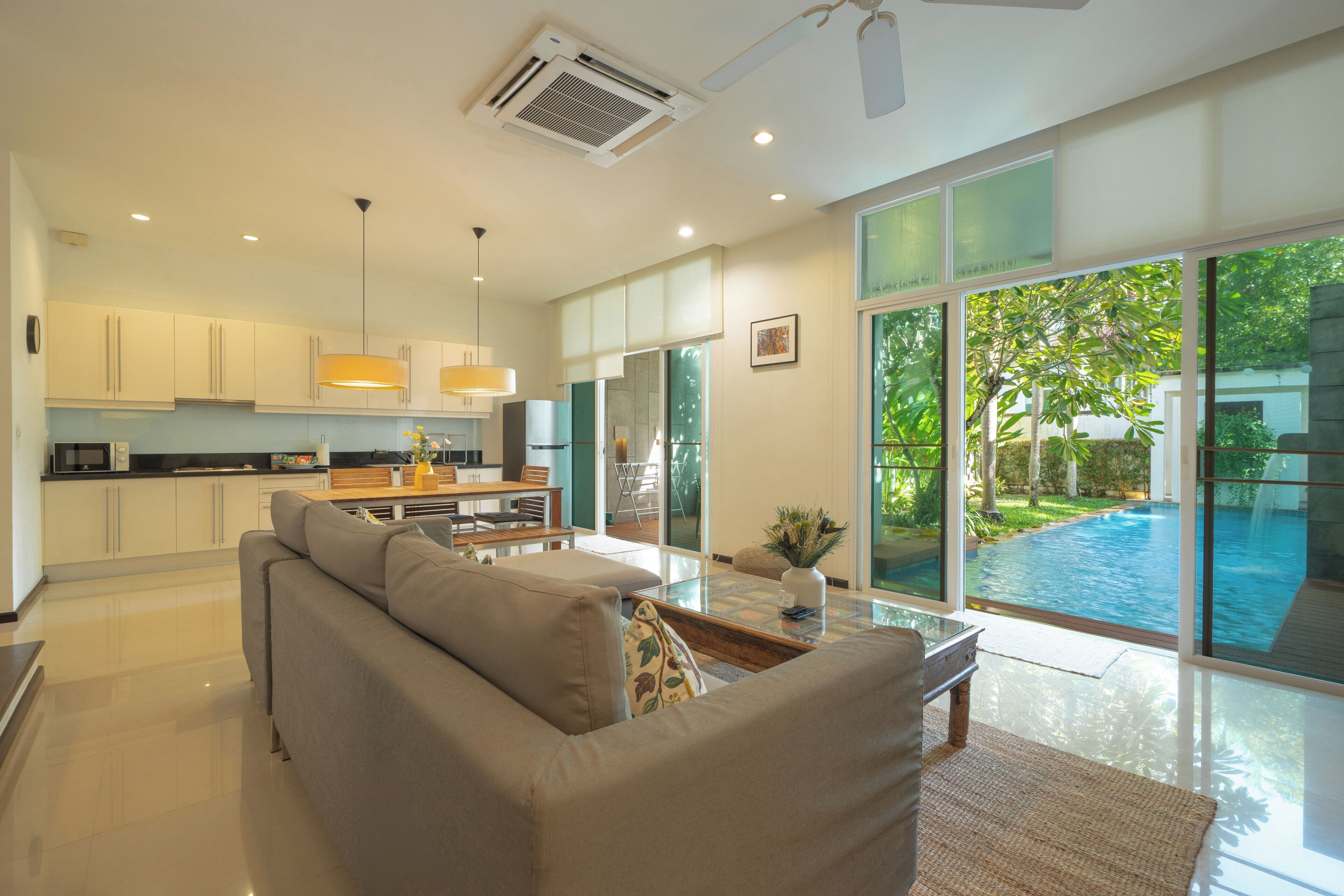 A modern kitchen with white cabinets, a dining area with a glass table, and a view of a swimming pool.