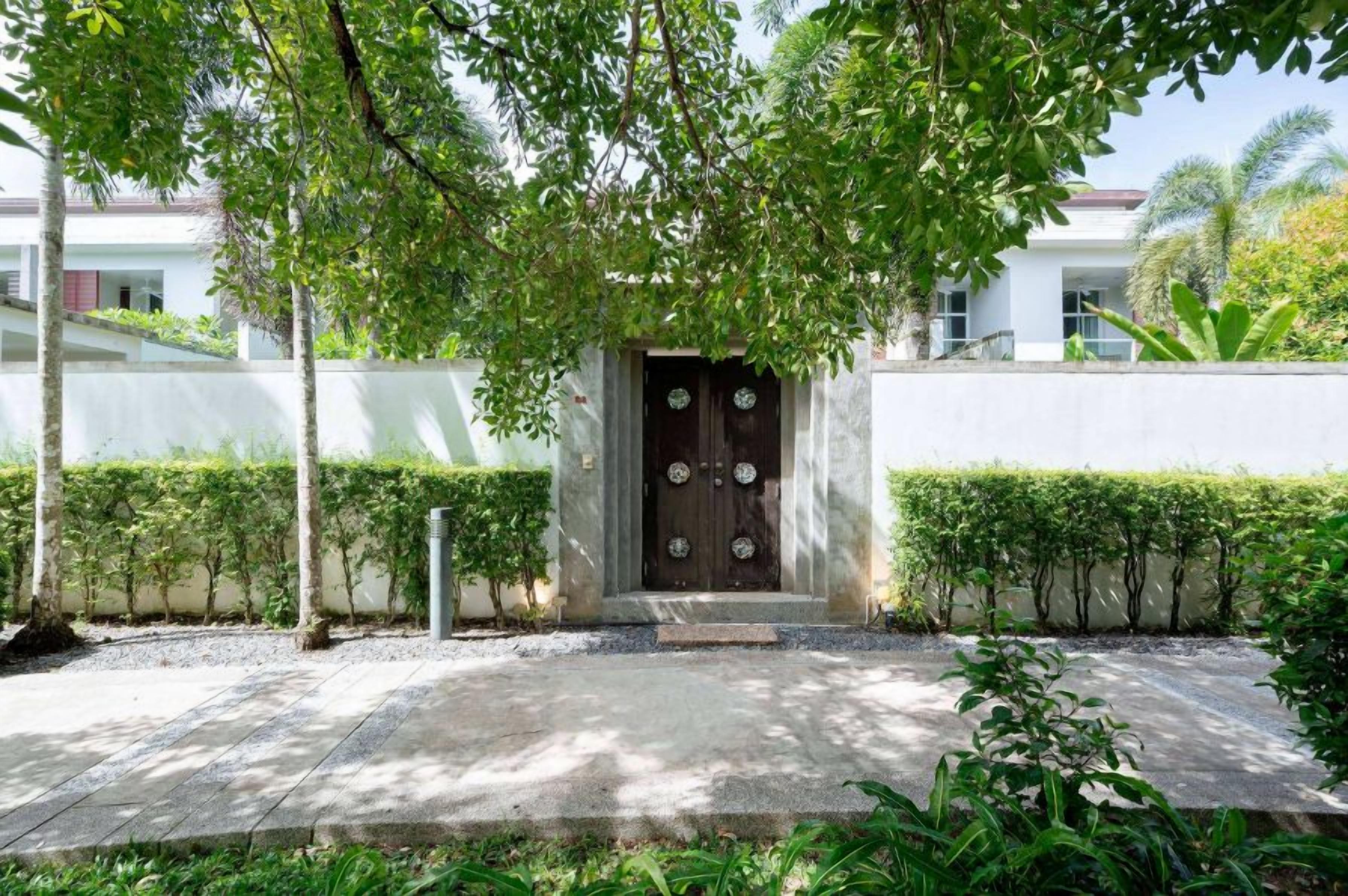 A building entrance with a dark door, a concrete pathway, and a well-maintained hedge.