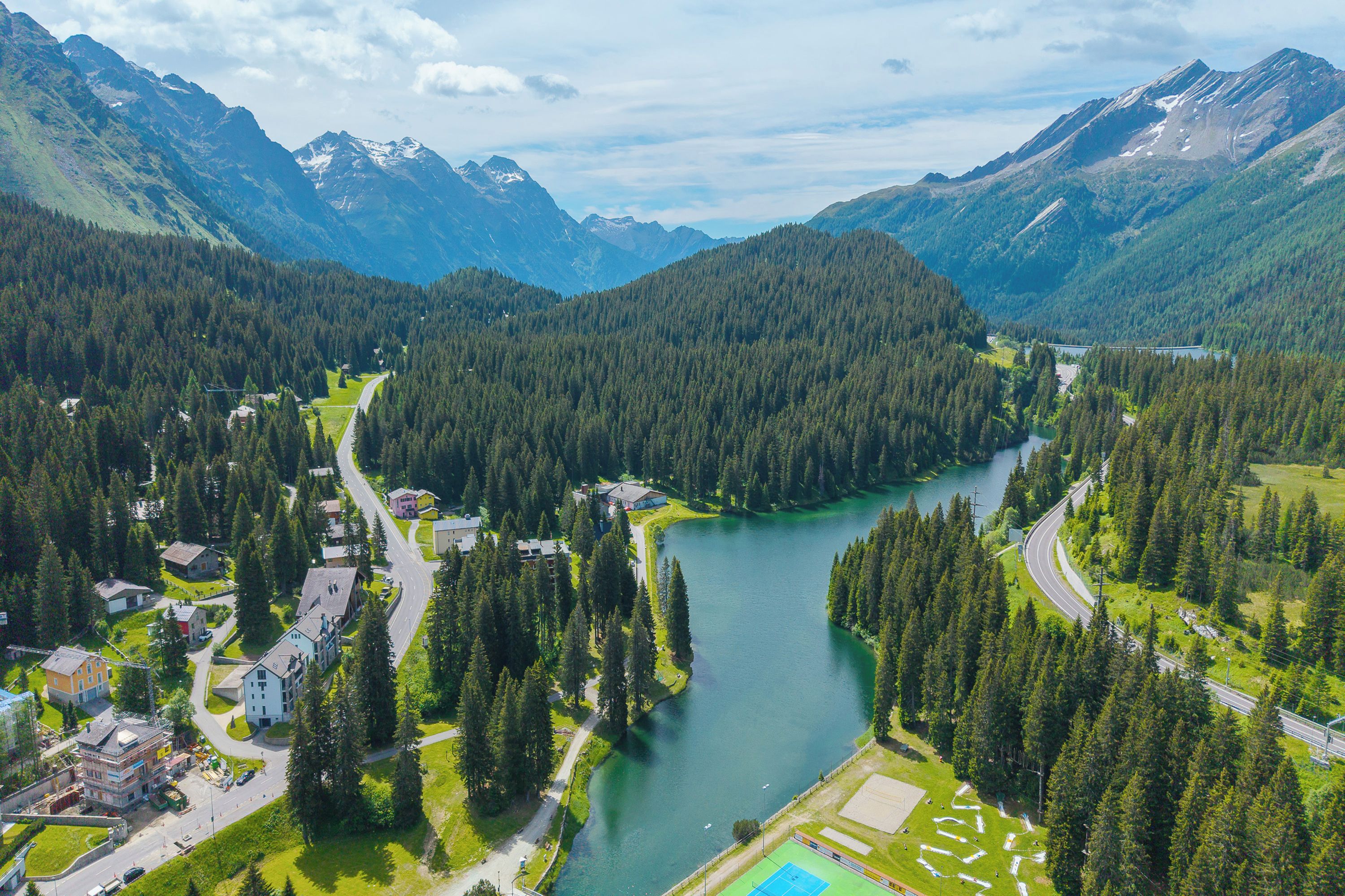 Un paysage montagneux avec une rivière, des routes et des bâtiments.