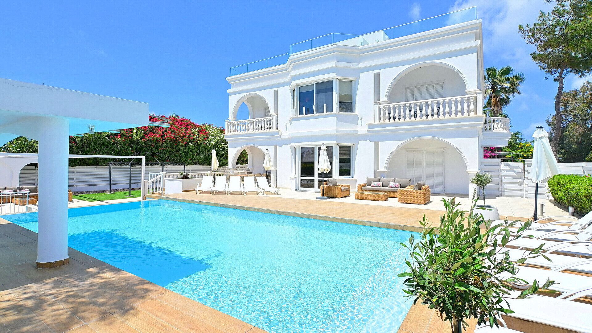 A large white building with a swimming pool, outdoor seating, and a covered patio area.