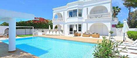 A large white building with a swimming pool, outdoor seating, and a covered patio area.