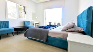 A modern bedroom with a bed, two chairs, a small table, and a view of the outdoors. - Villa Cecilia Coral - Beautiful Mansion in Coral Bay (Coral Bay)