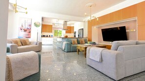 Un salon moderne avec un téléviseur à écran plat, deux canapés, une table basse et une cuisine en arrière-plan.