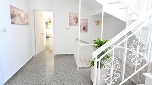 A hallway with a staircase leading to a landing, a door at the end, and a plant on the landing. - Villa Cecilia Coral - Beautiful Mansion in Coral Bay (Coral Bay)