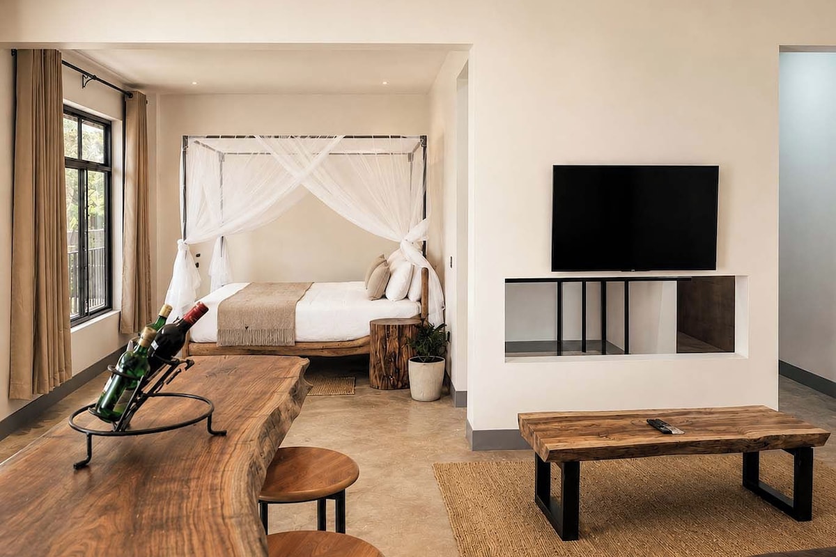 A modern hotel room with a bed, a TV mounted on the wall, a wooden coffee table, and a window with curtains.