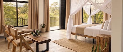 A bedroom with a bed, a seating area with chairs, a coffee table, and a view of greenery outside.