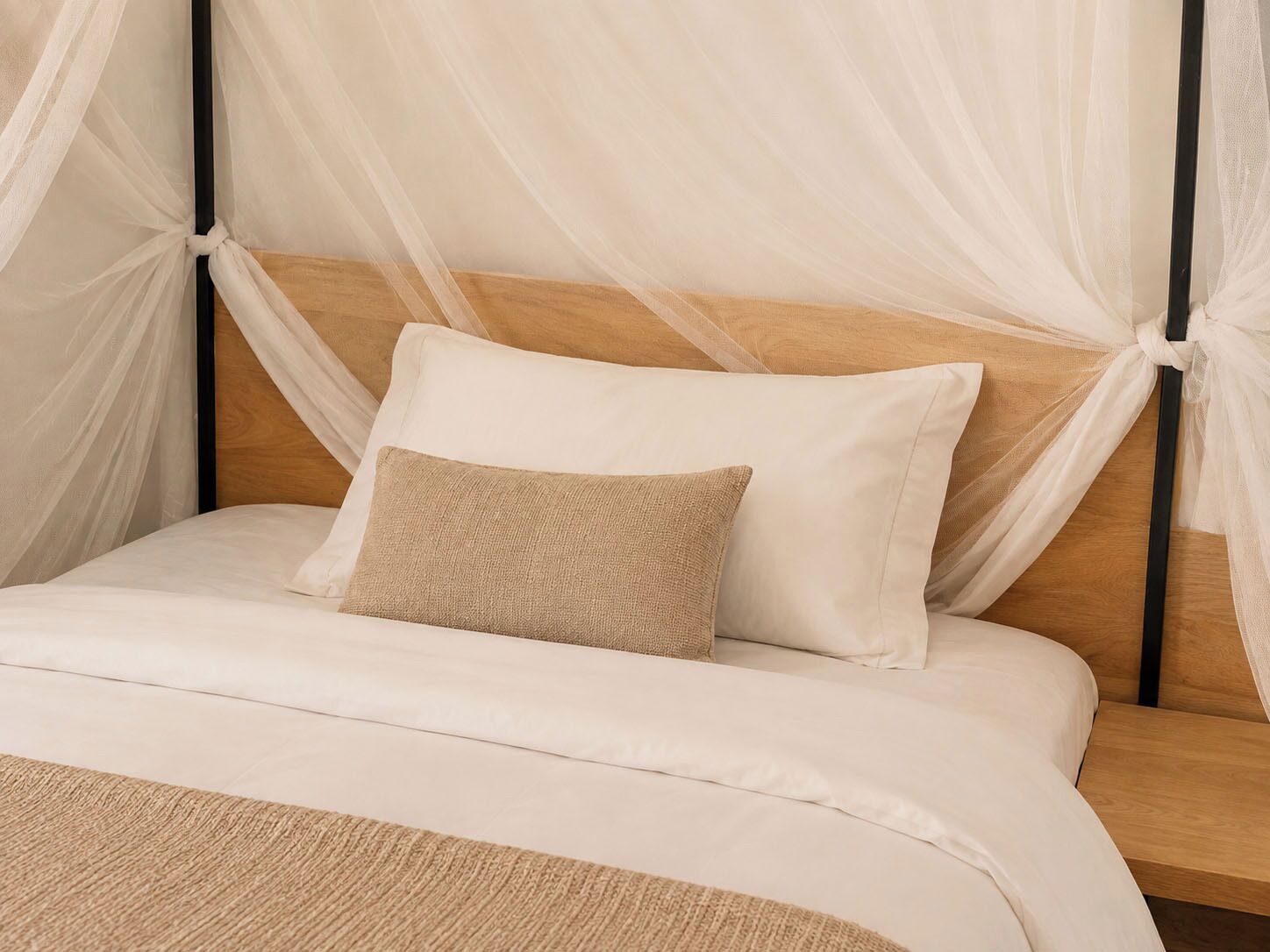 Una cama con cabecera de madera, ropa de cama blanca y almohada color beige.