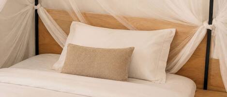 A bed with a wooden headboard, white bedding, and a beige pillow.