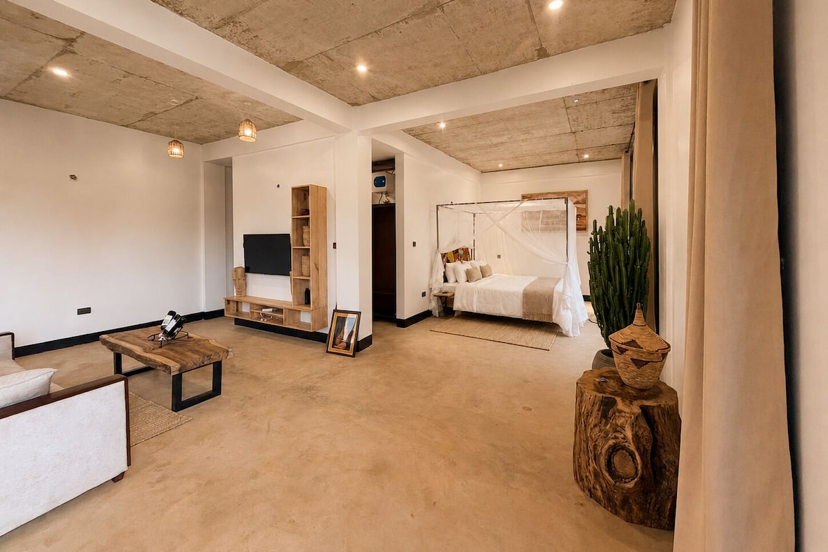 A spacious room with a large bed, a seating area with a sofa and a coffee table, and a television mounted on the wall.
