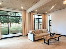 Una sala de estar moderna con un sofá, una mesa de centro y ventanas amplias con cortinas.