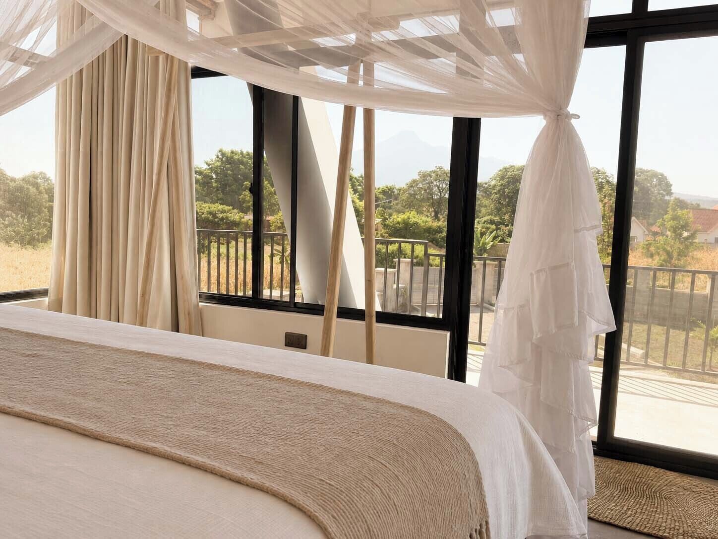 Un dormitorio con una cama grande, cortinas translúcidas y vistas al exterior.